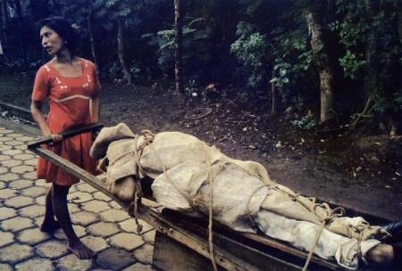 A woman pushes a cart containing the body of her husband, the remains to be buried in her back yard.